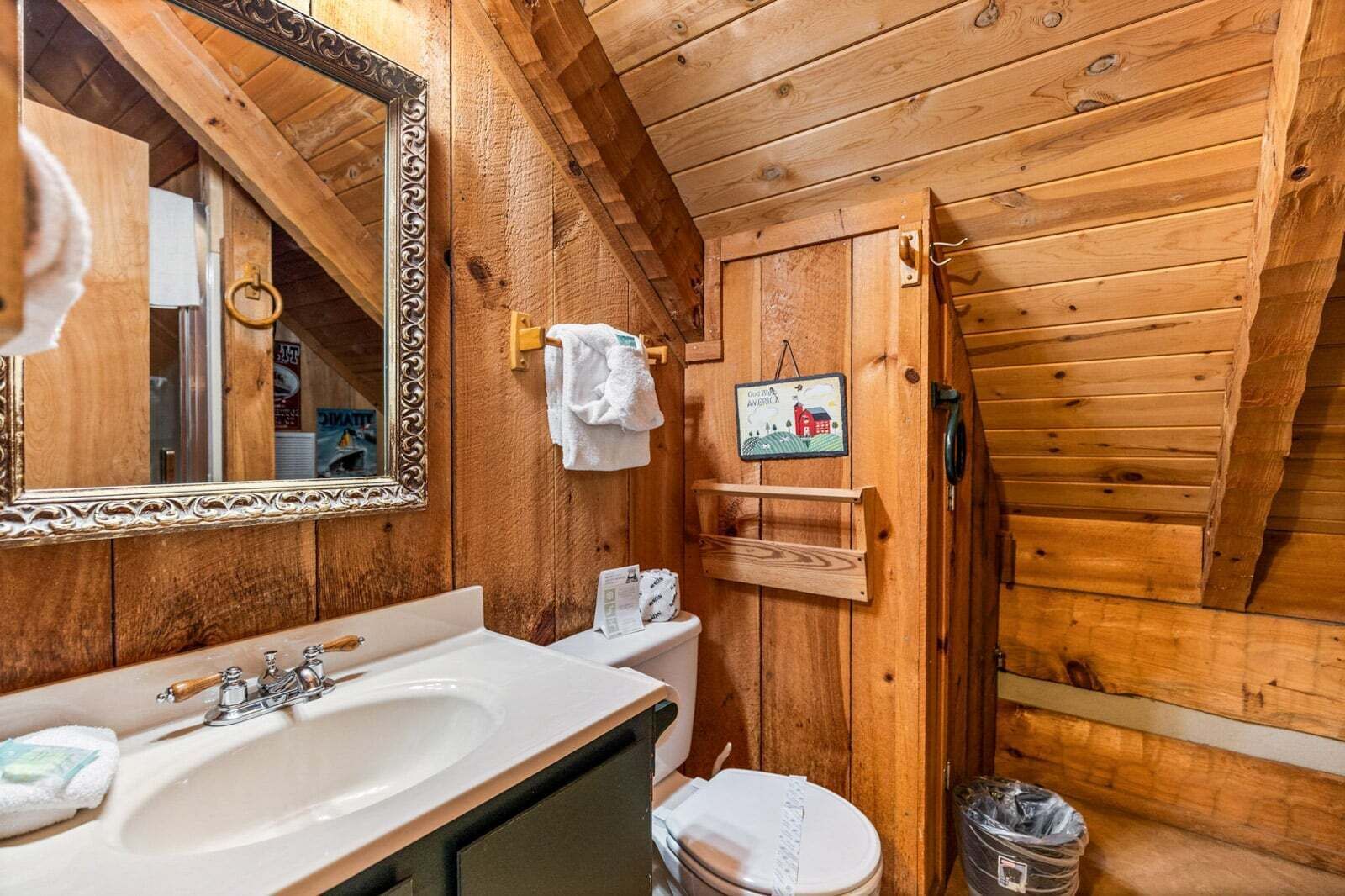 Ein Badezimmer einer Holzhütte mit Waschbecken, Spiegel, Toilette und Handtuchhalter.
