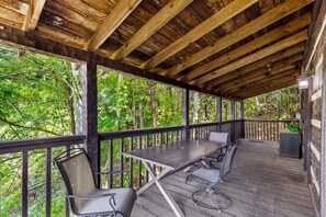 Un espace extérieur abrité, doté d’une table et de chaises, entouré d’une terrasse en bois et d’une forêt.