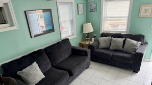 Ein Wohnzimmer mit zwei dunklen Sofas, einem Holzstuhl, einem kleinen Tisch mit einer Lampe und einem gerahmten Bild an der Wand.