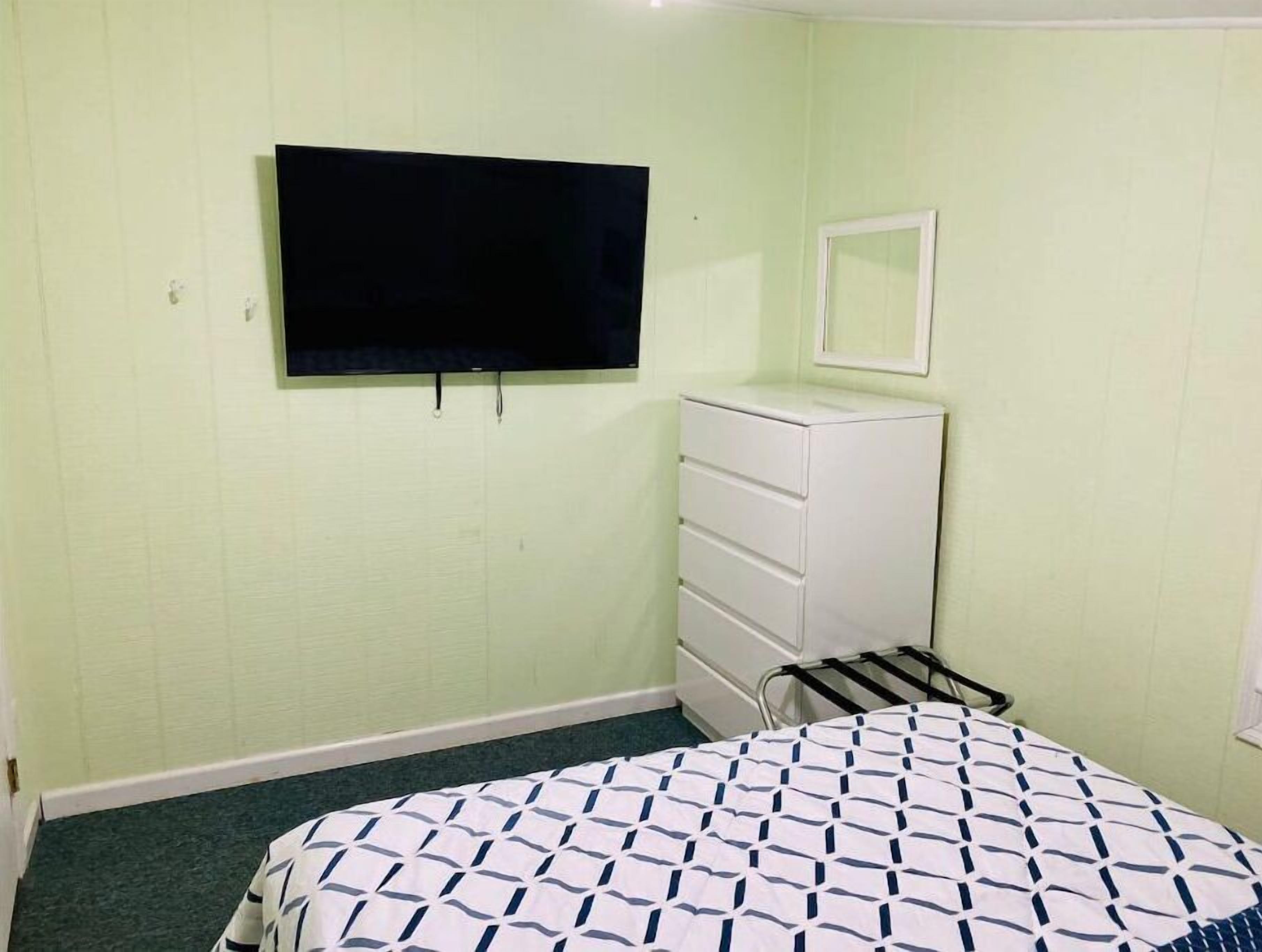 A room with a bed, a dresser, a television mounted on the wall, and a mirror above the dresser.