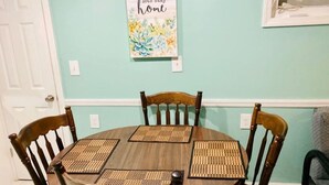 A dining table with four chairs, a wall-mounted picture, and a door. - Relaxing Ocean Block Retreat - Unbeatable Location, Free Parking, Outdoor Shower (Seaside Heights)