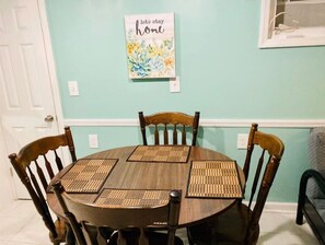 Uma mesa de jantar com quatro cadeiras, um quadro na parede e uma porta.