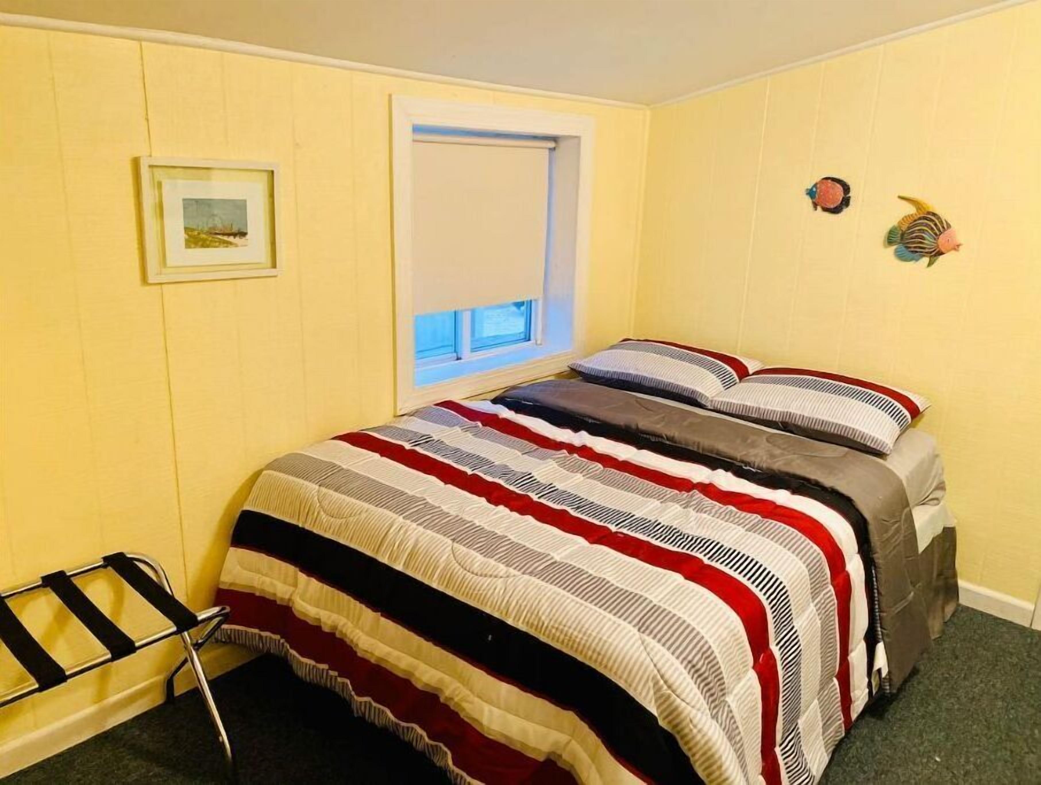 Um quarto com cama, janela, quadro na parede e uma pequena estante com objetos decorativos.