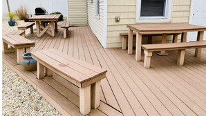 Eine Holzterrasse mit Picknicktischen und einem Grill.