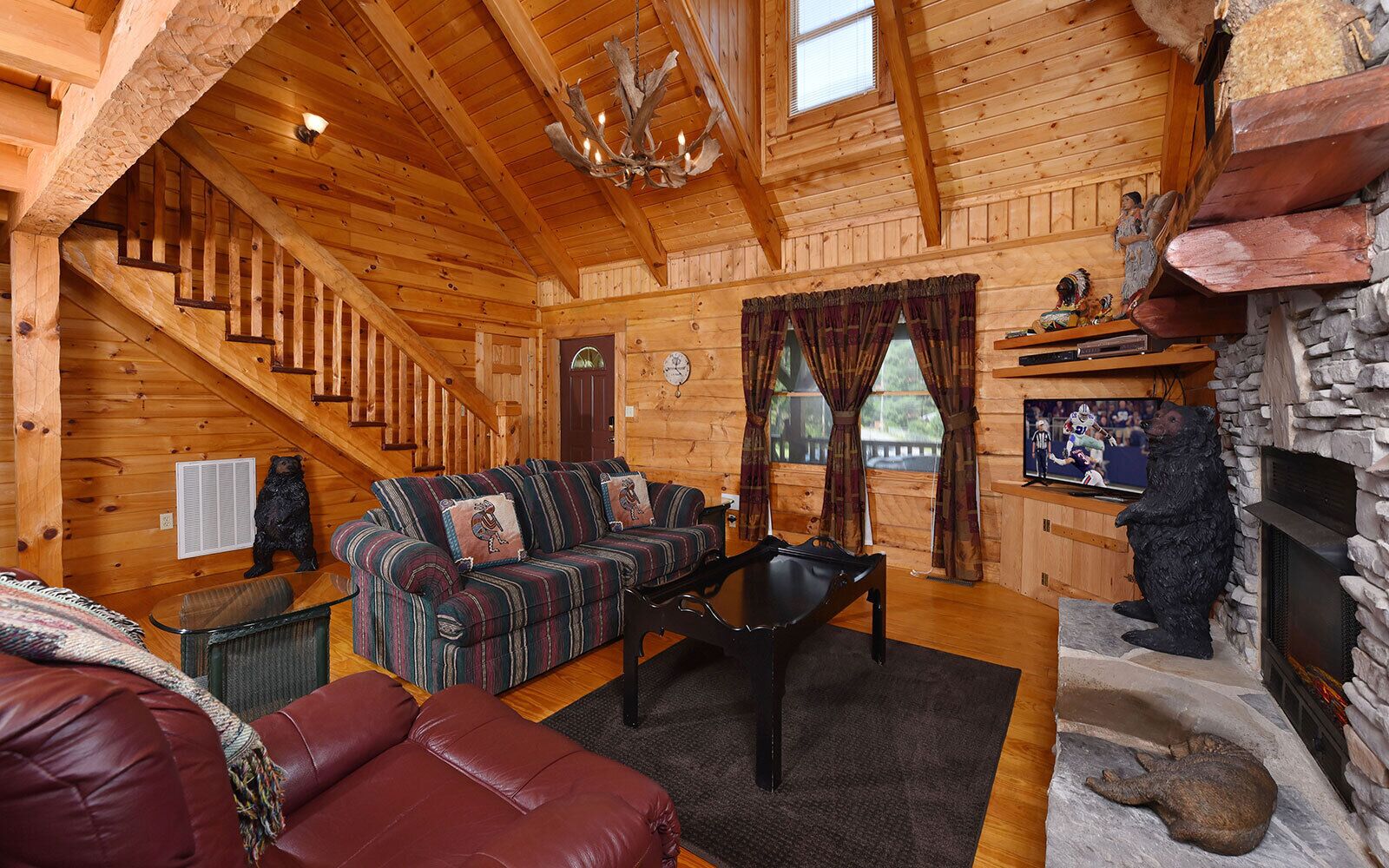 A log cabin interior with a staircase, a sofa set, a fireplace, and a television.