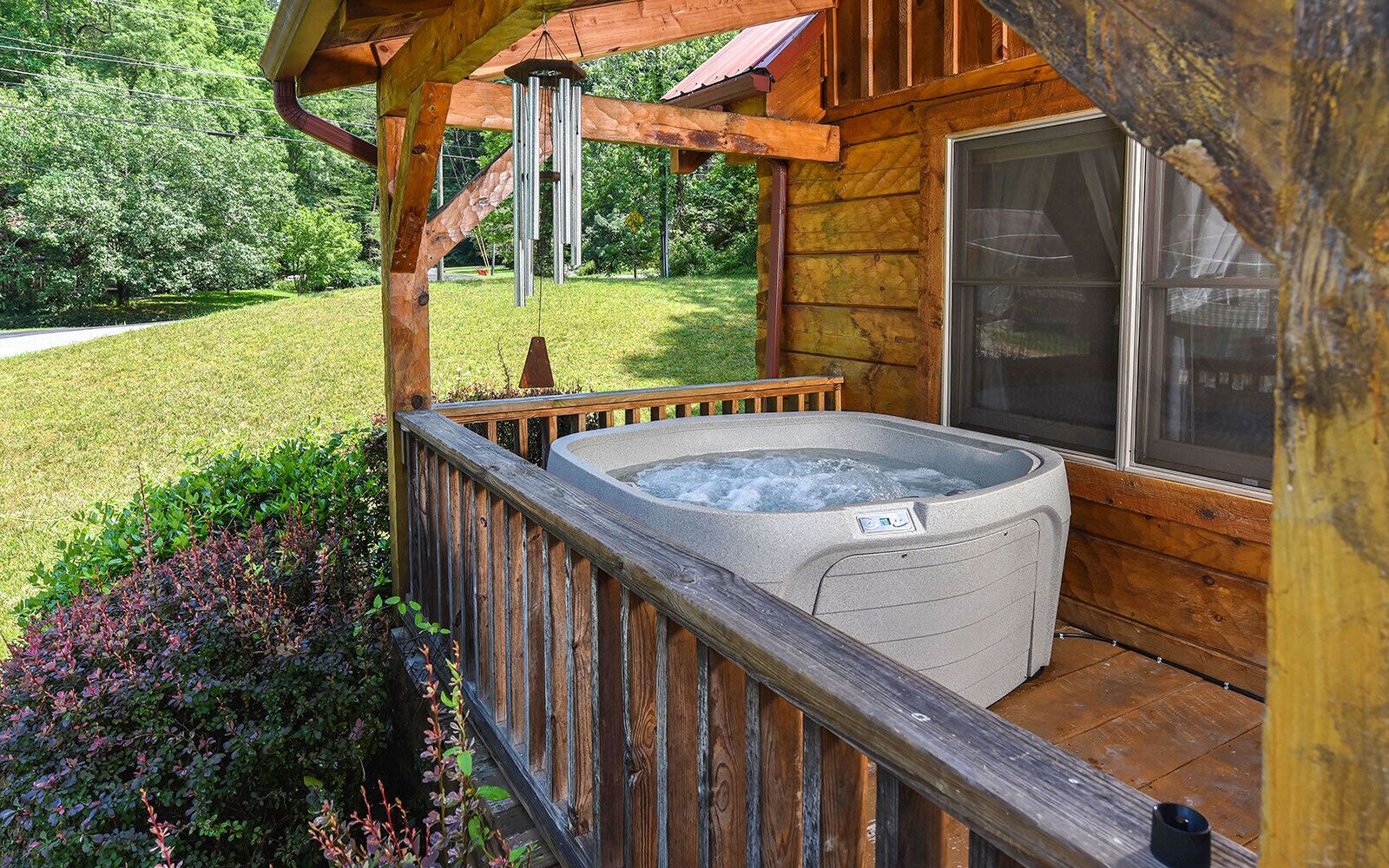 A hot tub on a wooden deck with a view of a grassy yard and trees.