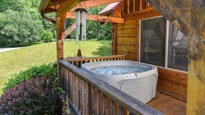 Un jacuzzi en una terraza de madera con vista a un jardín césped y árboles.