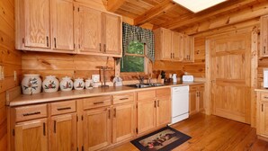 Una cocina tipo cabaña de madera con armarios de madera, un lavavajillas y una ventana con cortina a cuadros.