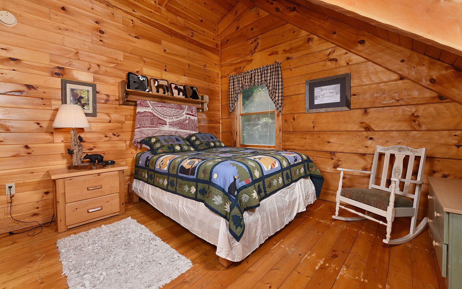 Ein gemütliches Schlafzimmer in einer Blockhütte mit einem hölzernen Bett, einem Schaukelstuhl, einem Nachttisch und einem Fenster mit karierten Vorhängen.
