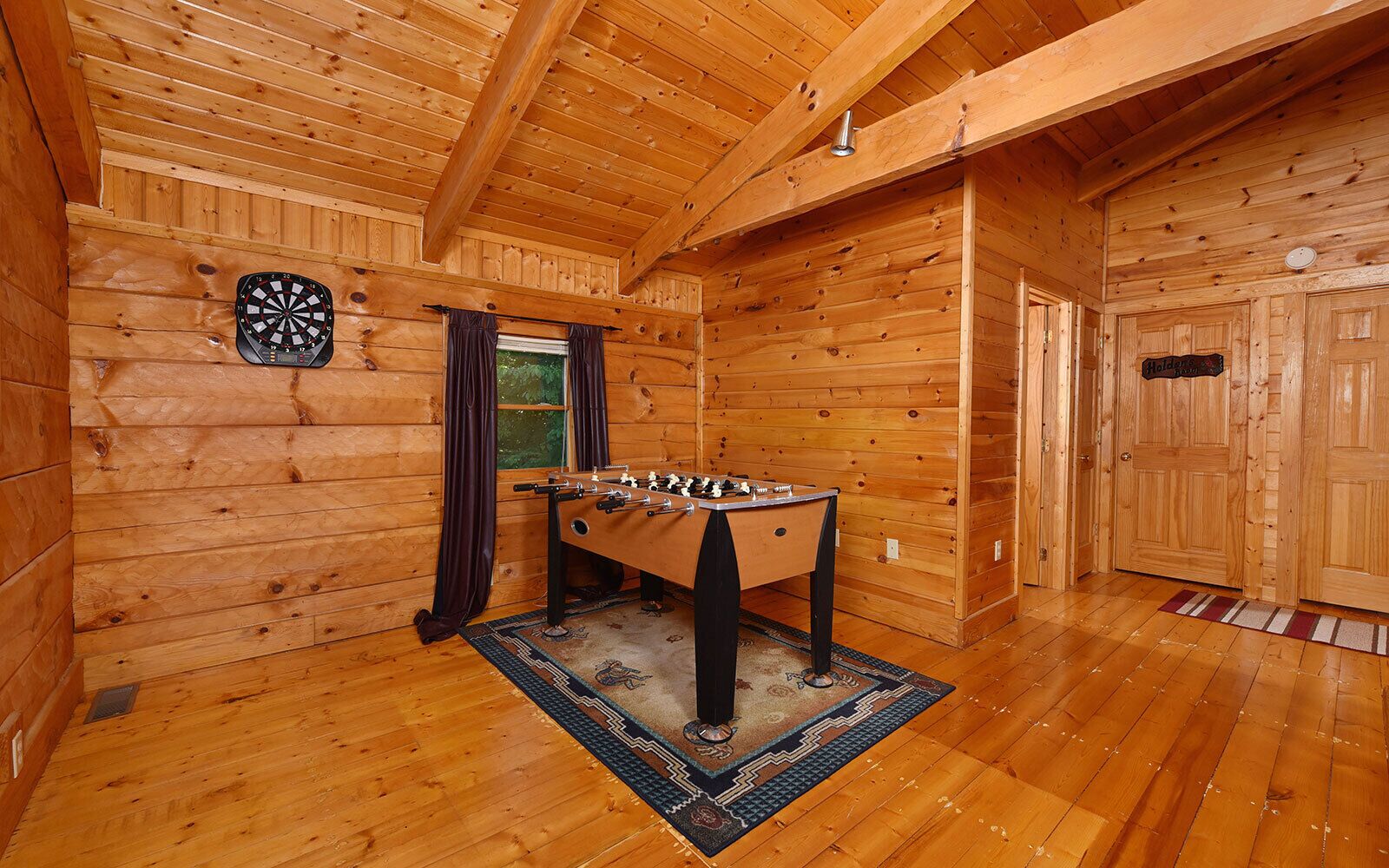 A cozy room with wooden walls and floors, a dartboard, and a foosball table.