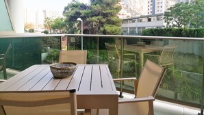 Un balcon avec une table et des chaises, un panier en osier et une vue sur une montagne et des bâtiments.
