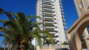 Un immeuble moderne et imposant, doté de nombreux balcons, avec un palmier au premier plan.