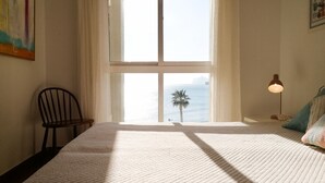 Une chambre avec une grande fenêtre, un lit, une chaise, une lampe et une vue sur la mer.