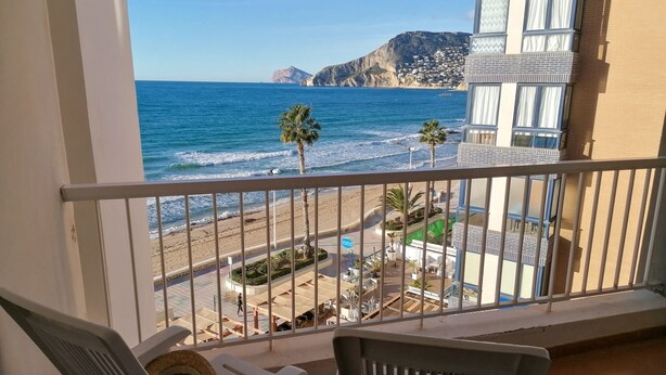 Un balcon avec vue sur la plage, les palmiers et une montagne en arrière-plan.
