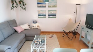 Un salon avec un canapé gris, une table basse blanche agrémentée d’objets décoratifs, un téléviseur posé sur un meuble et un fauteuil.