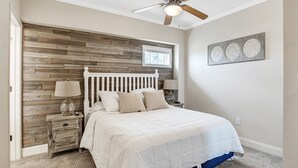 Una camera da letto con testiera in legno, un letto con biancheria bianca, due lampade da comodino, una ventola a soffitto e una finestra con tende.