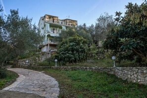Stunning residential building with a light green facade and balconies, set amidst lush greenery and a stone pathway.