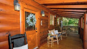 A wooden cabin with a porch, furnished with chairs and a bench, and decorated with a wreath and lanterns. - Ever After - Community Pool, Spa Tub, Pool Table, Hot Tub, & Smart TV! (Sevierville)