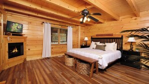 A cozy log cabin bedroom with a bed, a fireplace, a ceiling fan, and a television. - Ever After - Community Pool, Spa Tub, Pool Table, Hot Tub, & Smart TV! (Sevierville)