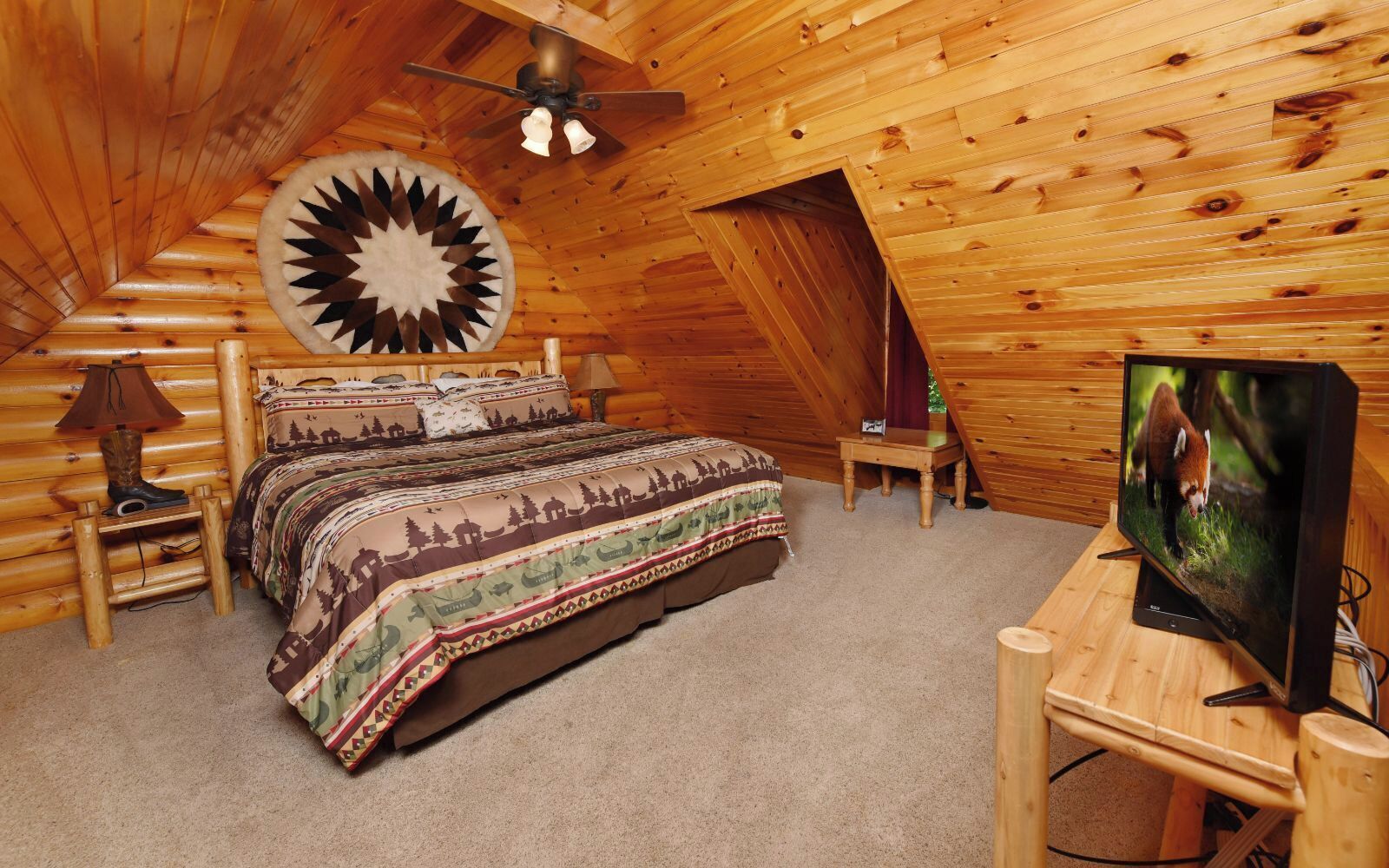 A cozy log cabin bedroom with a bed, a television, and a ceiling fan.