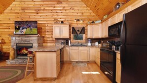 A log cabin interior with a stone fireplace, wooden cabinets, a kitchen with a refrigerator, stove, and microwave. - Think a Little Less - Air Hockey, Gas Fireplace (Sevierville)