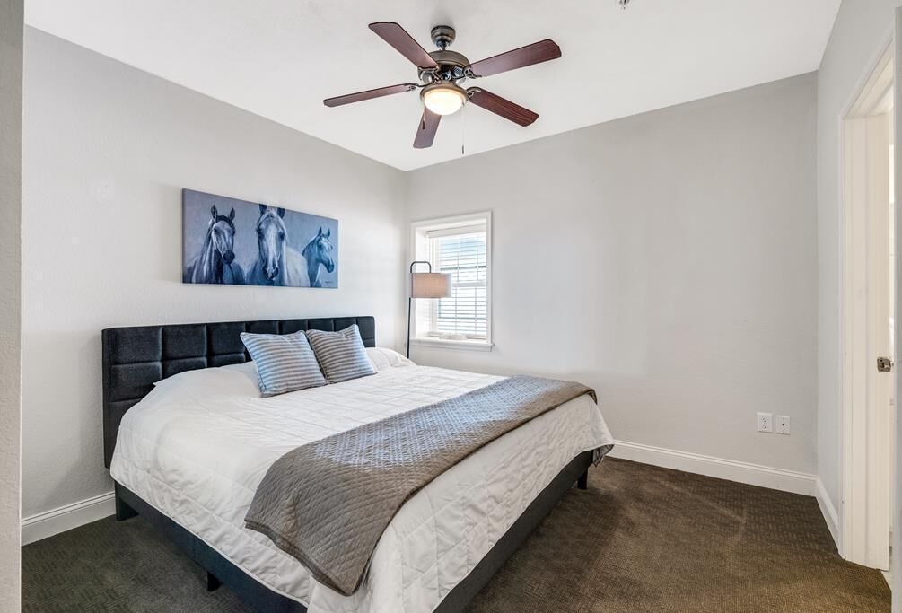 A bedroom with a bed, a ceiling fan, a window with blinds, and a painting on the wall.