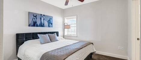 A bedroom with a bed, a ceiling fan, a window with blinds, and a painting on the wall.