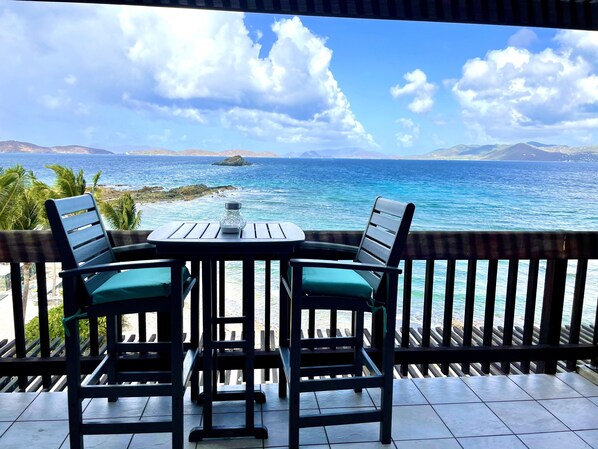 A table and chairs on a balcony with a view of the ocean and distant mountains.