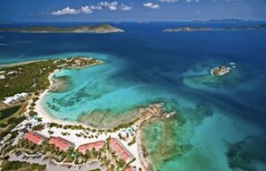 An aerial view of a coastal resort with clear turquoise waters, a sandy beach, and a small island with buildings.