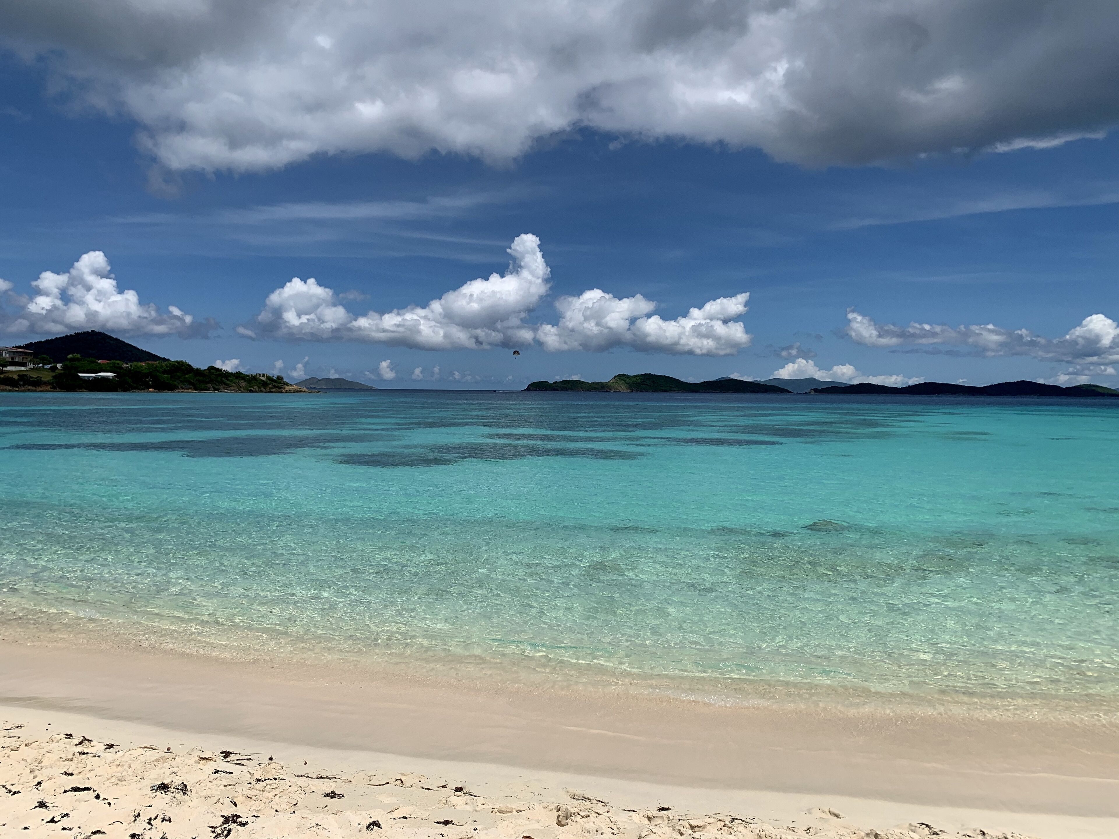 En strand med kristallklart turkost vatten, en sandstrand och avlägsna öar under en delvis molnig himmel.