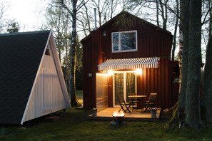 Een houten vakantiehuis met een overdekt terras, een vuurkuil en een tafel met stoelen.