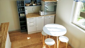 Une cuisine compacte dotée d’un plan de travail en bois, d’un four encastré et d’un lave-vaisselle. On y trouve une table ronde avec deux chaises et un luminaire suspendu.