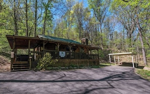 Situated in a wooded area, this cabin features a porch with a covered seating area and a sign reading 'Campsite You'.
