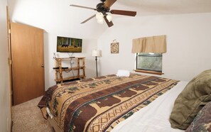 Relax in this inviting bedroom with a large bed, ceiling fan, and TV, plus a window offering a view of the outdoors.