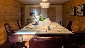 Ein Zimmer mit Holzwänden, einem langen Tisch, Ledersesseln, einer Hängeleuchte und Kunstwerken an den Wänden.