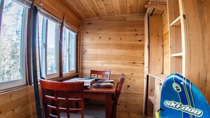 L’intérieur d’un chalet en bois, avec une table à manger, des chaises, des skis et des chaussures de ski.