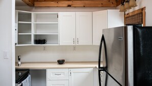 Une cuisine avec des meubles blancs, un réfrigérateur noir et un plafond en bois.