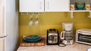 Una cocina con armarios blancos, una pared amarilla, un refrigerador blanco, un tostador, una cafetera y un microondas.