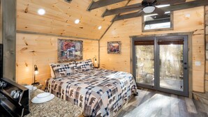 Une chambre confortable avec un lit, des murs en bois, un ventilateur de plafond et une porte-fenêtre coulissante donnant sur l’extérieur.