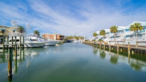 Marina com barcos atracados, um calçadão de madeira e edifícios com varandas e palmeiras.