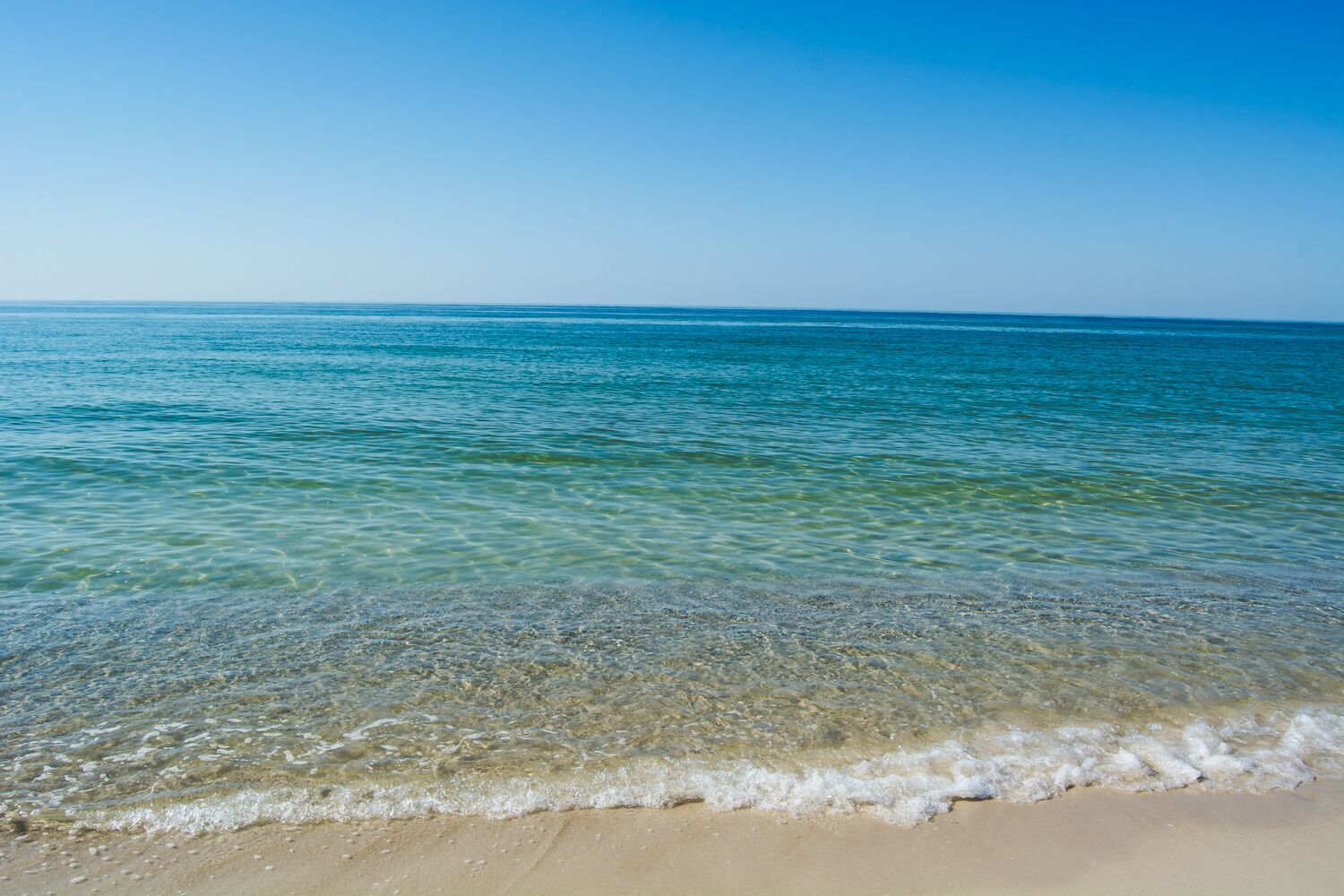 A beach with clear shallow waters and a sandy shore.