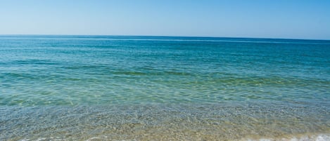 A beach with clear shallow waters and a sandy shore.