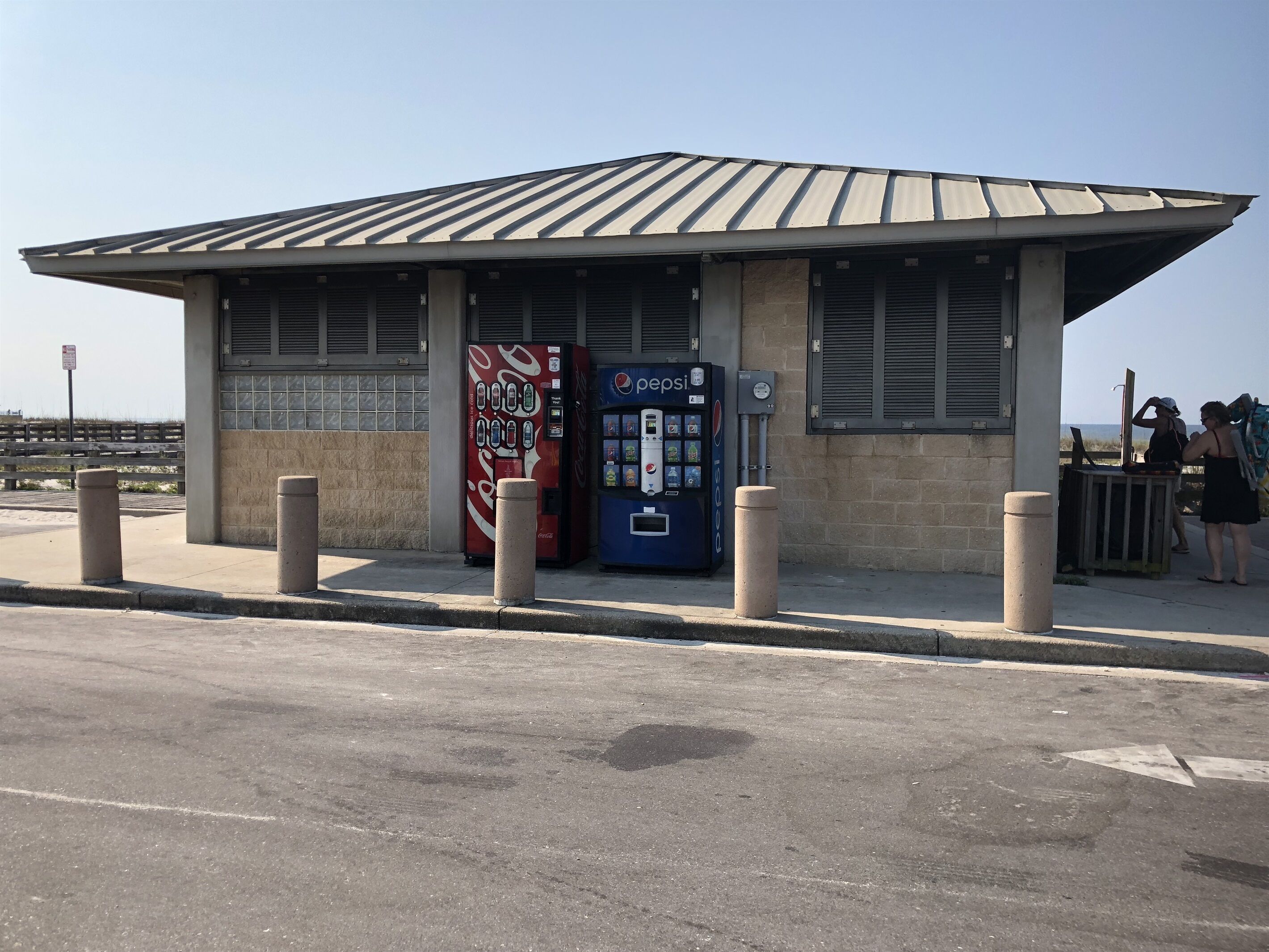 A small, single-story building with a flat roof and two vending machines, one Coca-Cola and one Pepsi, on its side.