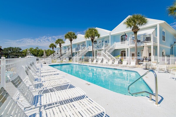 A poolside area with white lounge chairs, a swimming pool, and a building with balconies and palm trees.
