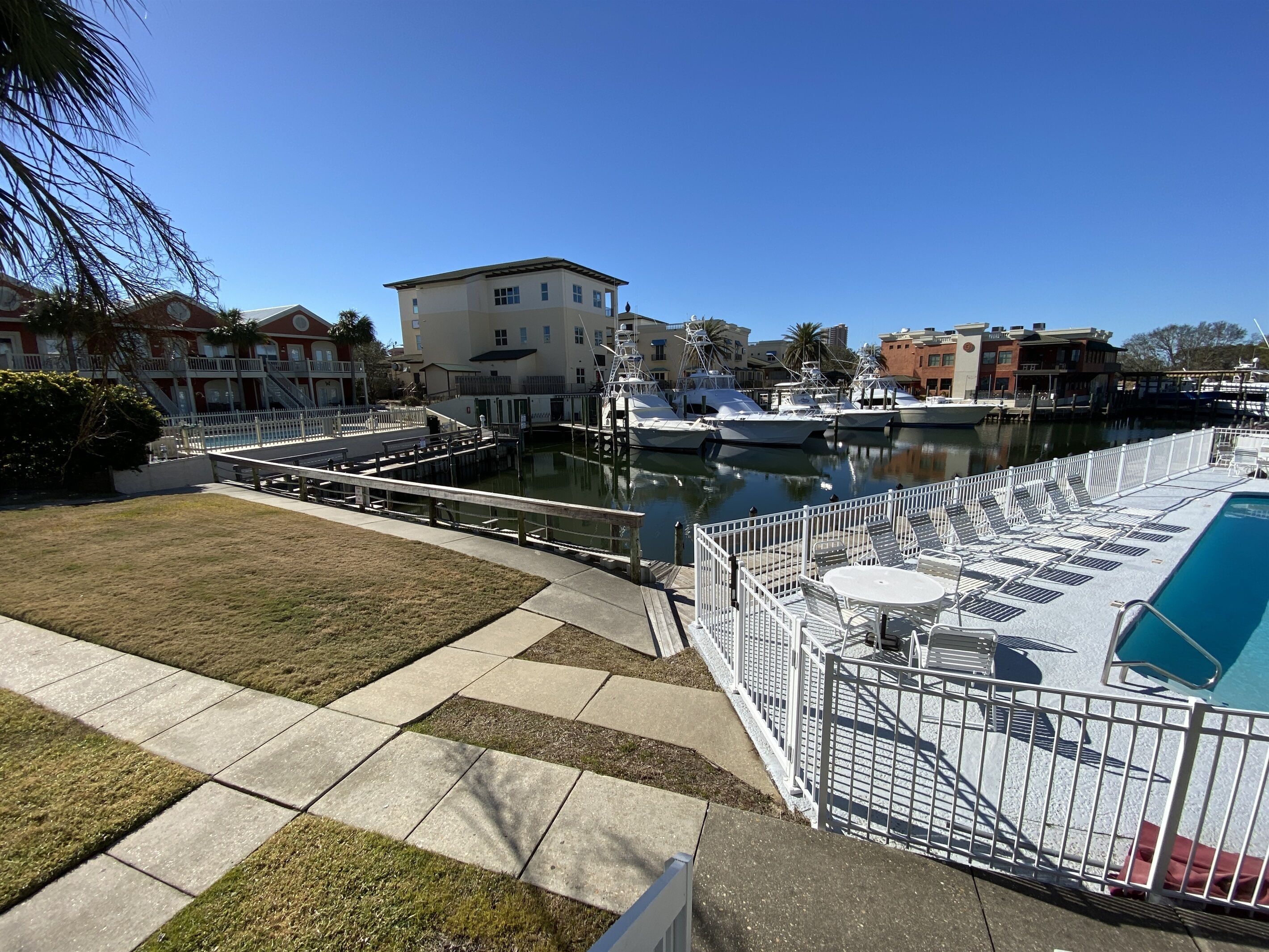 A marina with boats docked, a pool area with lounge chairs, and a grassy lawn.