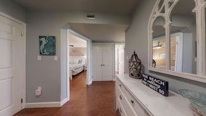 A hallway with a bed in the background, a mirror, a sign, and a decorative lantern. - Meticulously Decorated Gulf Front Unit at Jetty East! One FREE Beach Chair Setup (Destin)