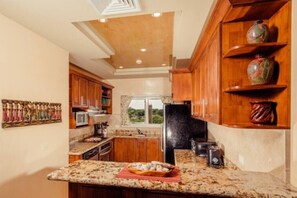 A kitchen with wooden cabinets, granite countertops, a black refrigerator, and decorative pottery on shelves.