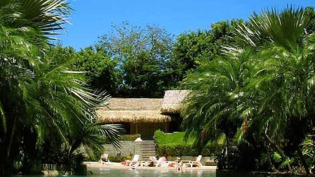A pool area with lounge chairs and a thatched-roof structure. - Matapalo 603☆ Oceanview, Huge Lagoon Pool, in the ♥ of Town ☆ (Tamarindo)