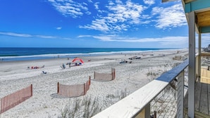 A beach view with a wooden deck and a building with a blue roof. - Decked Out - Newly Renovated Four-Bedroom, Two-Bath Oceanfront Beach House (Garden City Beach)