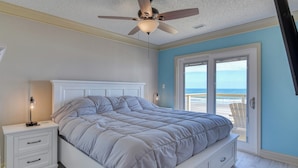 A bedroom with a bed, nightstand, lamp, ceiling fan, and a view of the ocean through a sliding door. - Decked Out - Newly Renovated Four-Bedroom, Two-Bath Oceanfront Beach House (Garden City Beach)